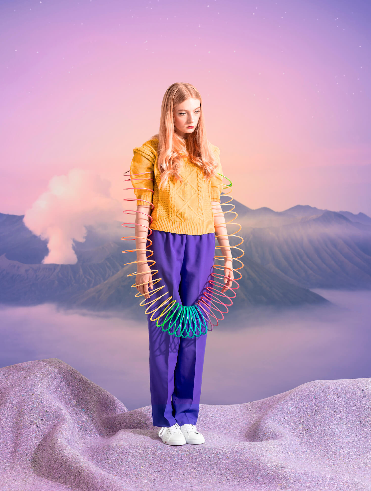 Young girl wrapped in slinky, standing amongst purple sand and mountain landscape.