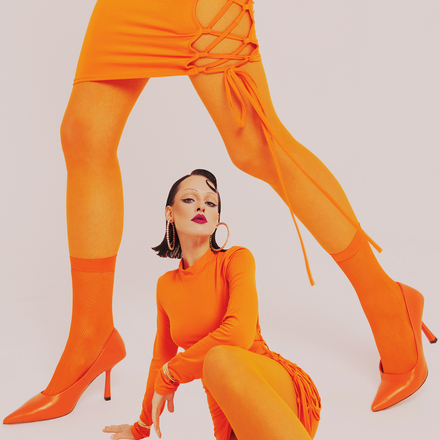 Woman wearing a orange monochrome outfit with legs towering over her.