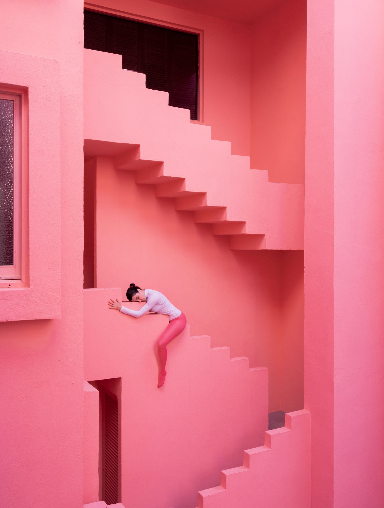 Photograph of artist laying ontop of staircase that belongs to bright pink building.