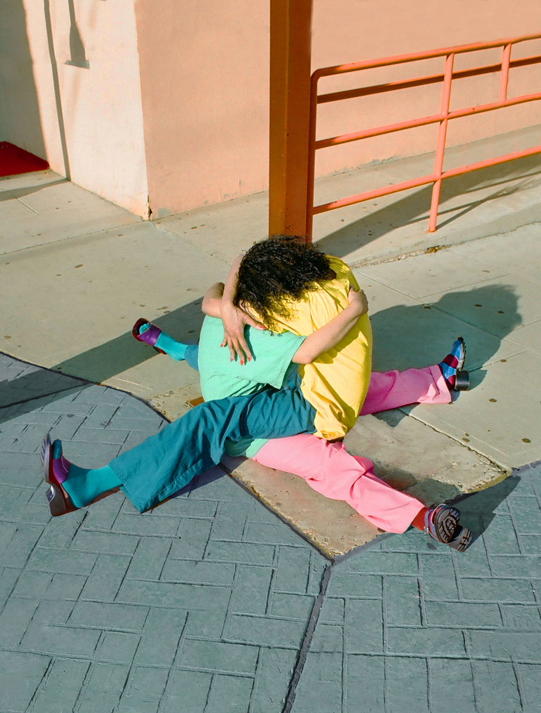 Two models sitting on the ground, embracing one another.