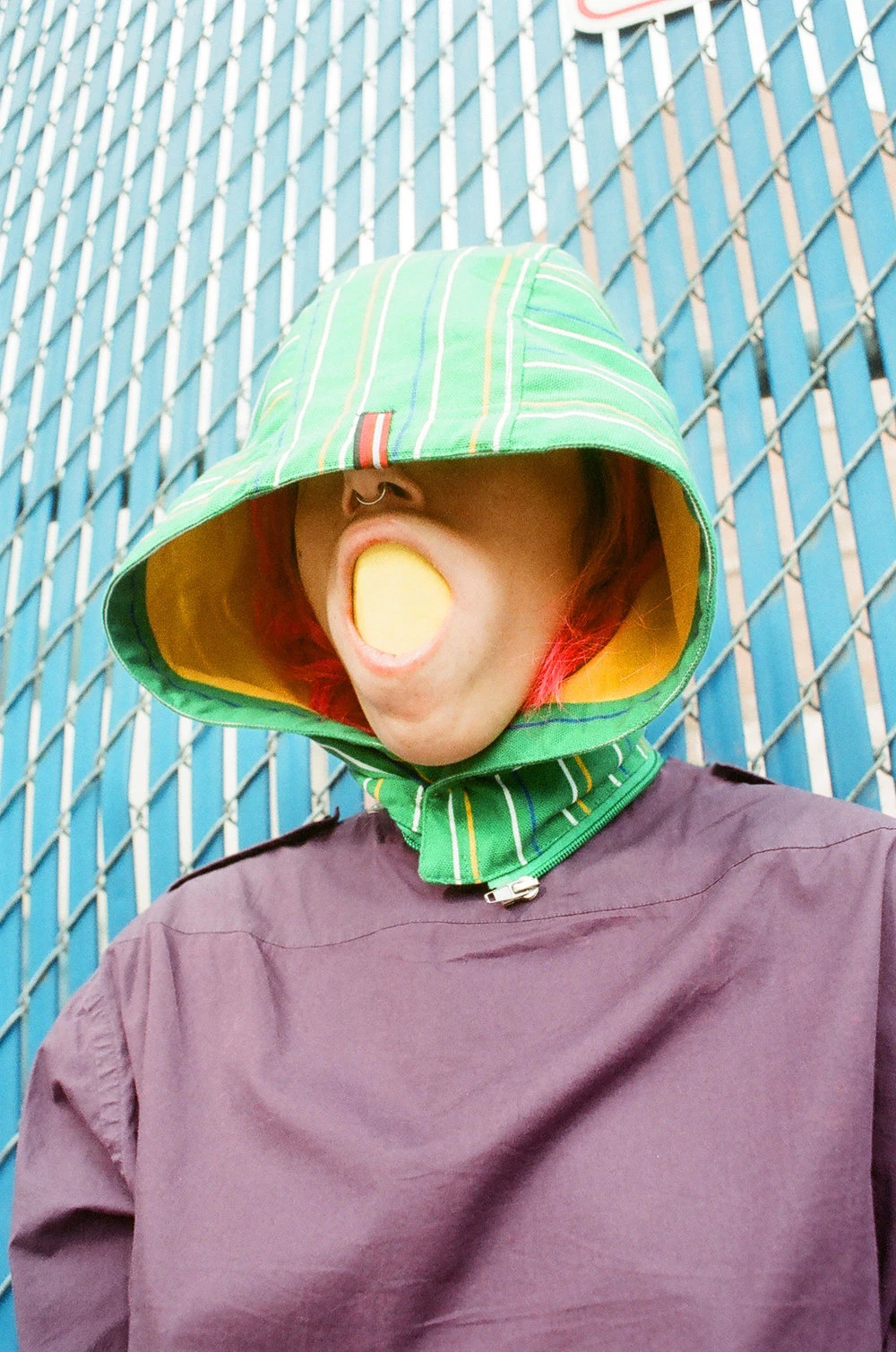 Model holding ball in mouth, wearing a hooded colorful raincoat.