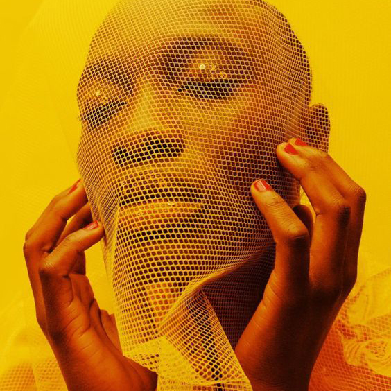 Woman's face drapped with yellow netted fabric.